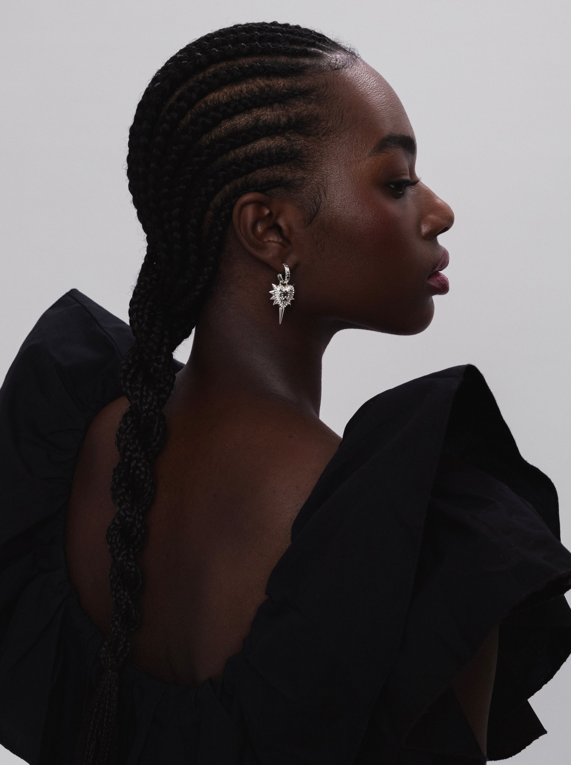 A close-up profile shot of a model wearing the Drama Queen Heart Spike Earring in silver, featuring a patterned heart charm with prominent spikes.
