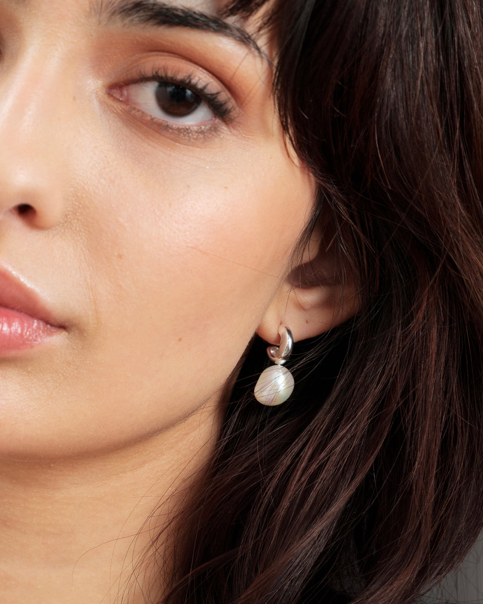Close-up of a model wearing the Paxton silver hoop earring with a dangling baroque freshwater pearl.