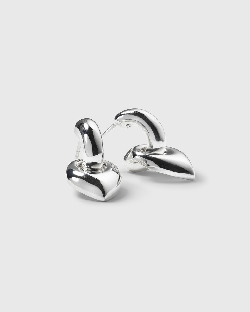 A product shot of the Melinda Earrings in silver, highlighting their bold design which features a chunky hoop and a dangling, leaf-shaped pendant.