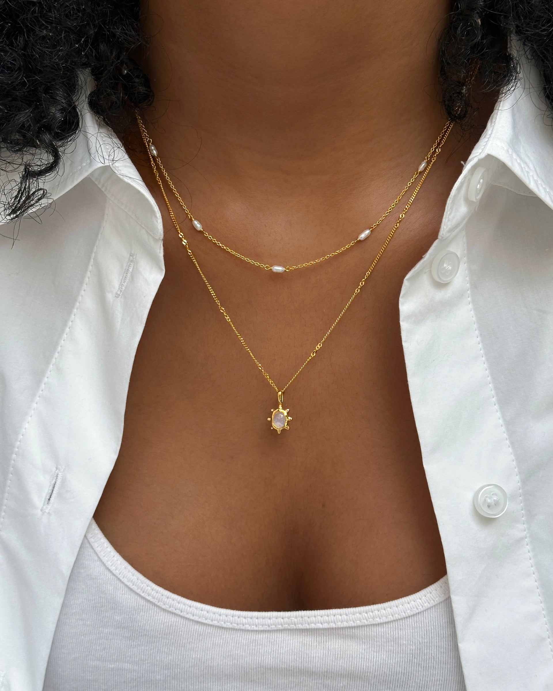 A close-up of a model wearing the Florentina Necklace with its gold flower-shaped moonstone pendant, layered with the delicate gold Treasure Multi Pearl Necklace.
