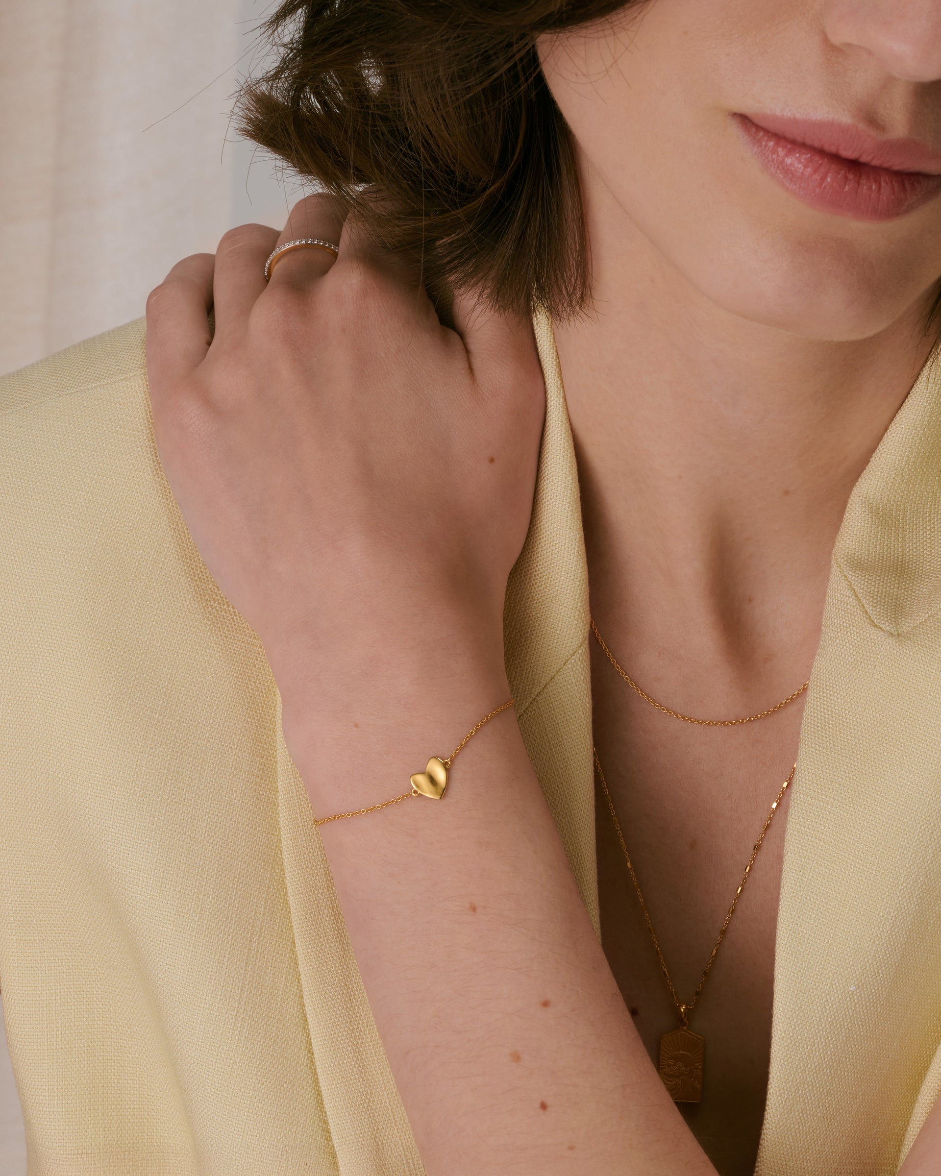 A delicate gold chain bracelet with a hammered heart charm, paired with a gold ring and two layered gold necklaces. 