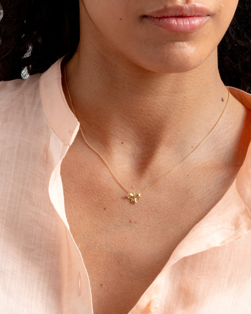 A close-up shot of a model wearing the Rosie Mini Necklace in gold, featuring a delicate chain and a small bow-shaped pendant.