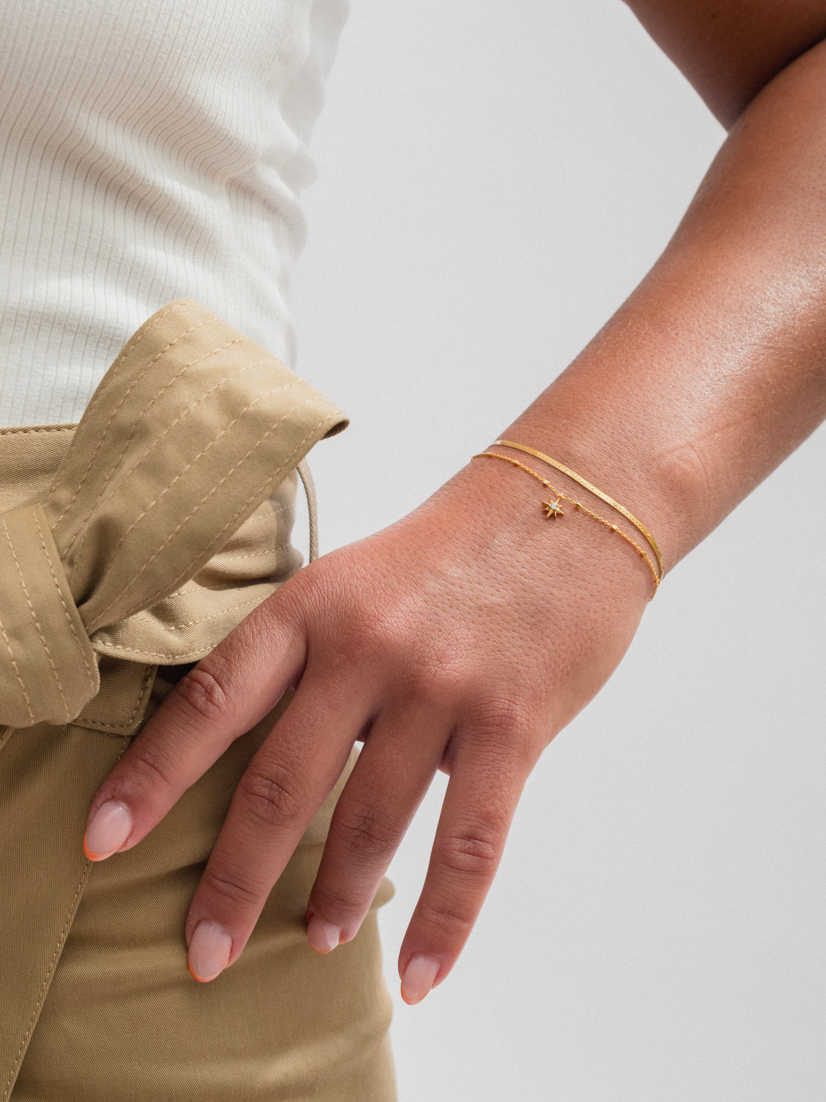 A model wearing the gold Herringbone Bracelet, a flat and smooth chain, styled with the delicate North Star Bracelet featuring a small star charm.