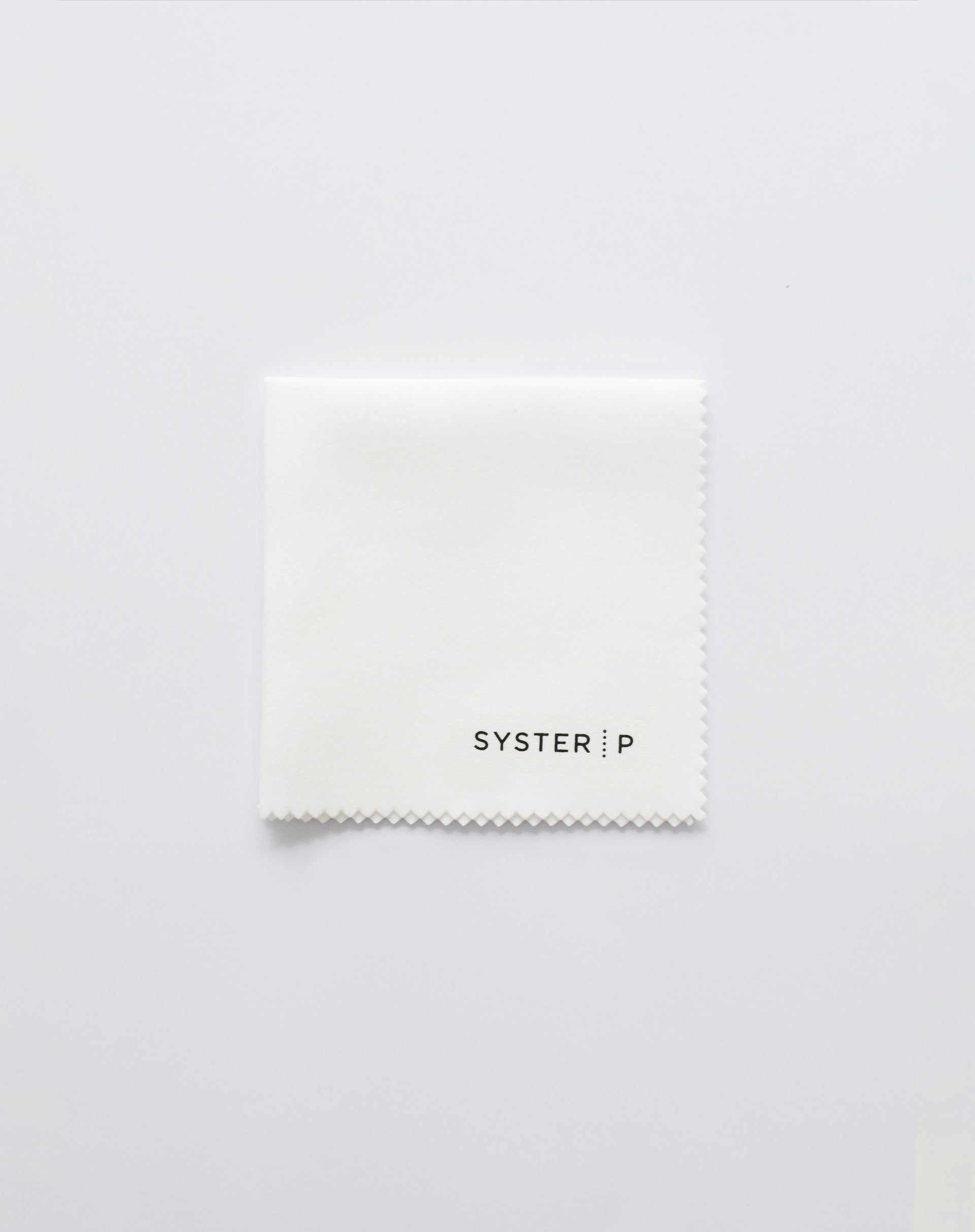 A product shot of the Syster P Polishing Cloth, a white, square cloth with zig-zag edges and the brand's logo in black.