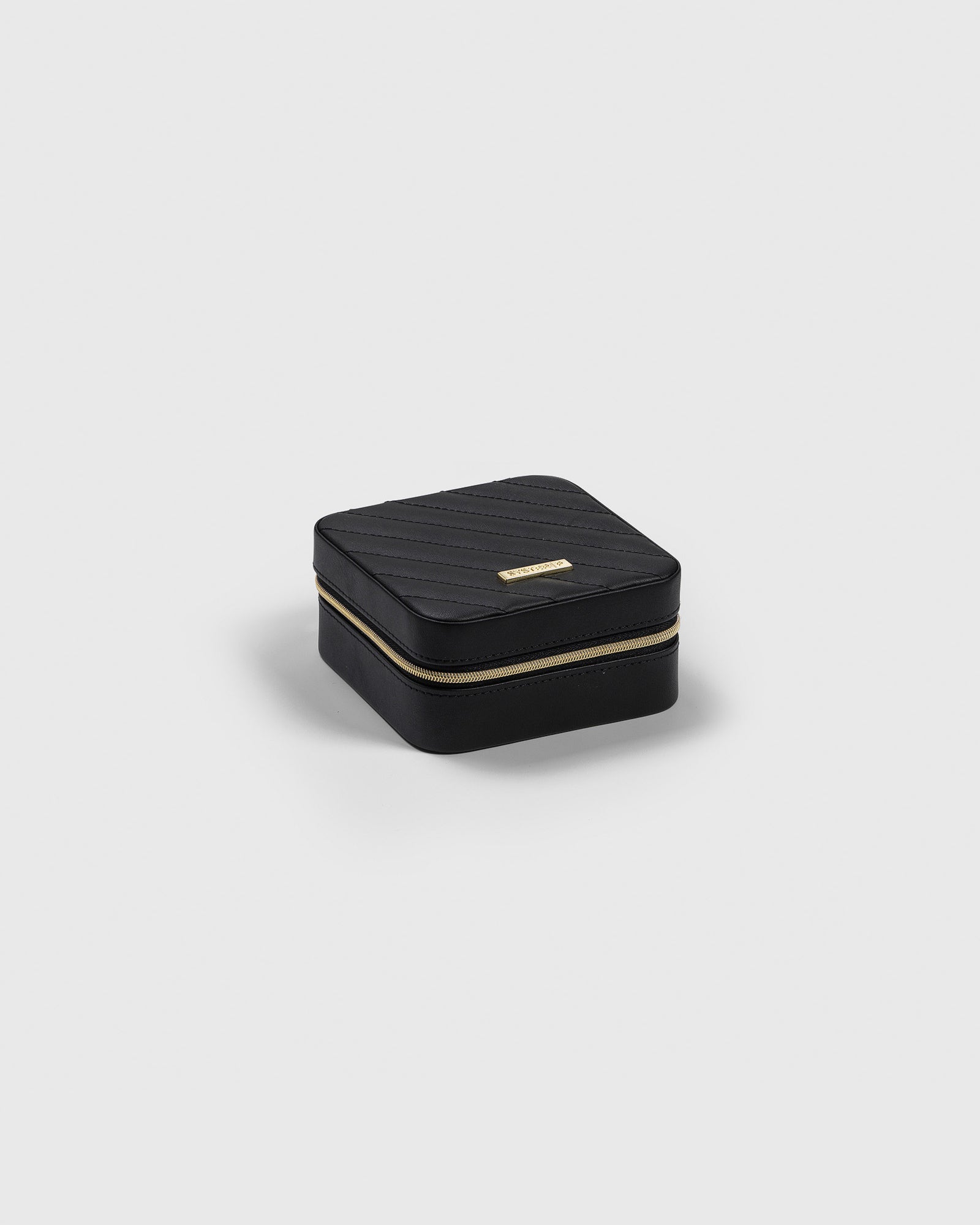 A product shot of the small, black Syster P jewelry case, showing its quilted top, gold zipper, and brand plaque.