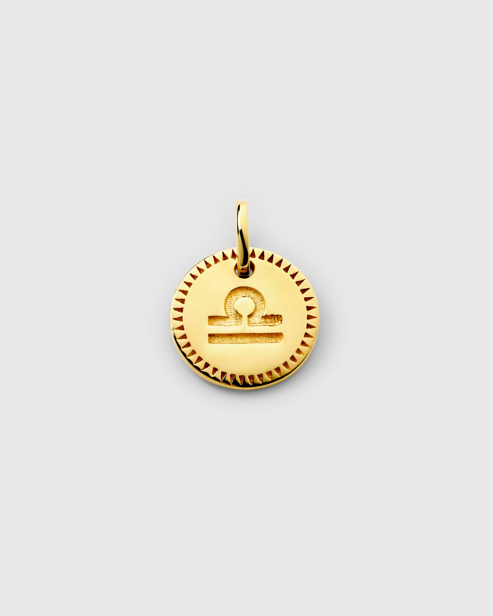 A close-up of the gold Beloved Zodie Pendant, showcasing the engraved Libra zodiac symbol on the circular charm, framed by a textured border.