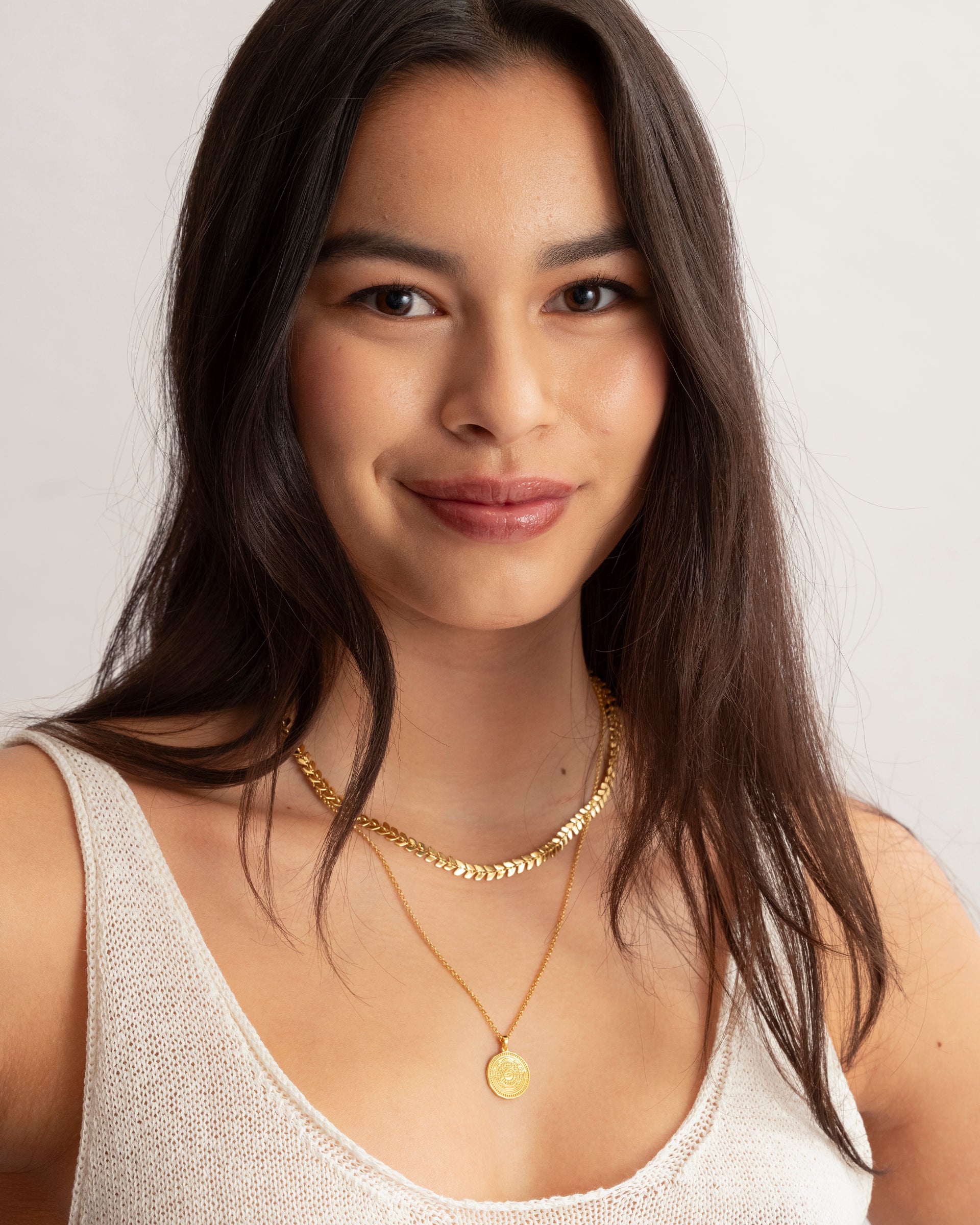A close-up of a model wearing the Lucky Coin Navigate Necklace in gold, featuring a compass pendant, layered with a thicker gold chain necklace.