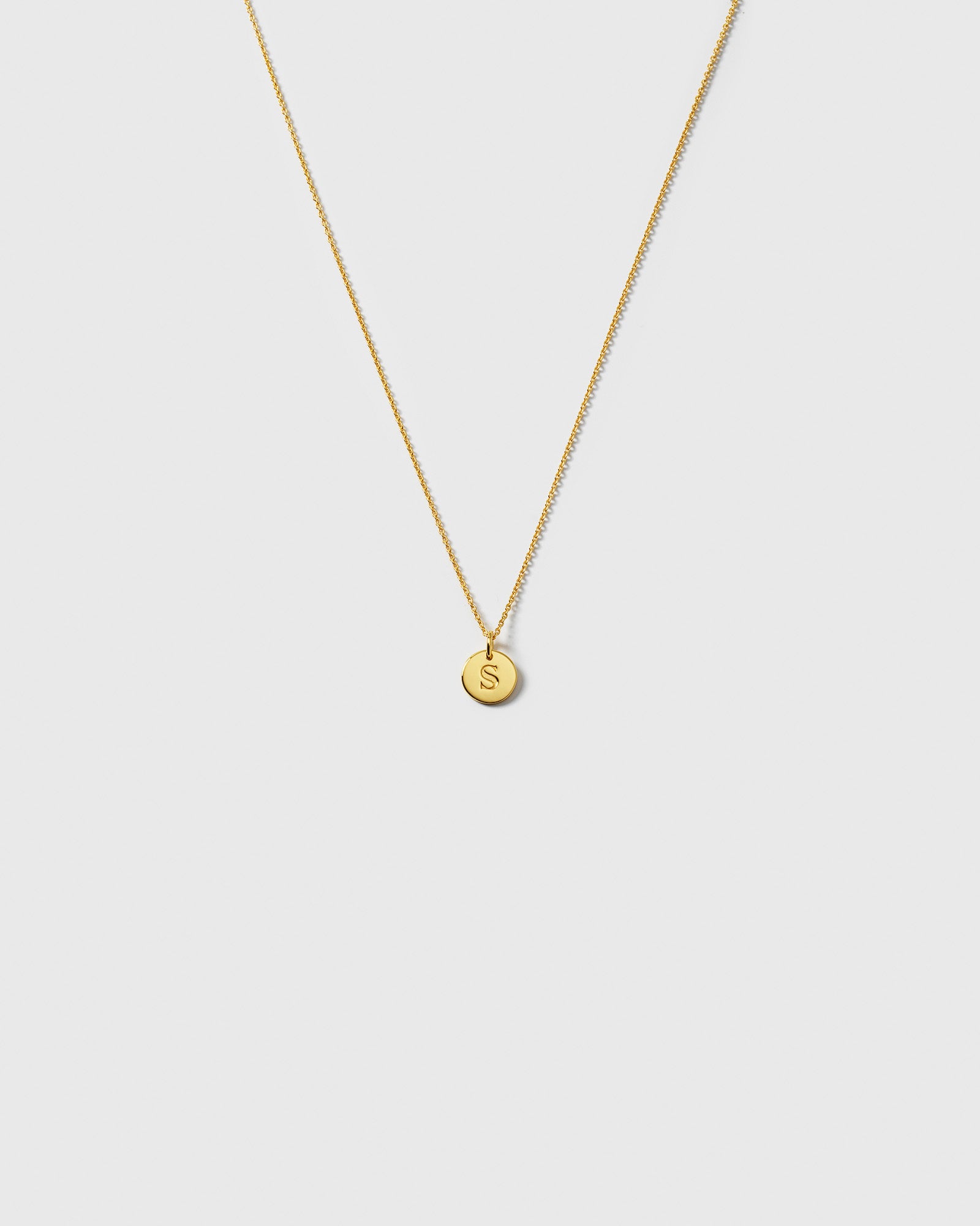 A product shot of the gold Beloved Short Oval Chain, styled with a small, circular pendant engraved with the letter 'S'.