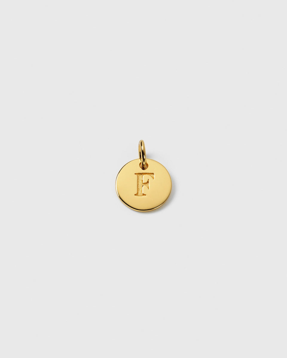 A product shot of the Beloved Mini Letter Gold pendant, featuring the letter 'F' engraved onto a small, round gold charm.