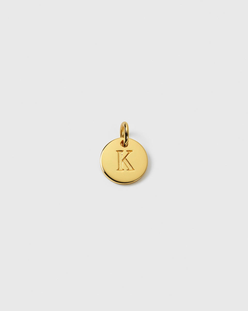 A product shot of the Beloved Mini Letter charm in gold, featuring a small, round pendant with the letter 'K' engraved on its surface.
