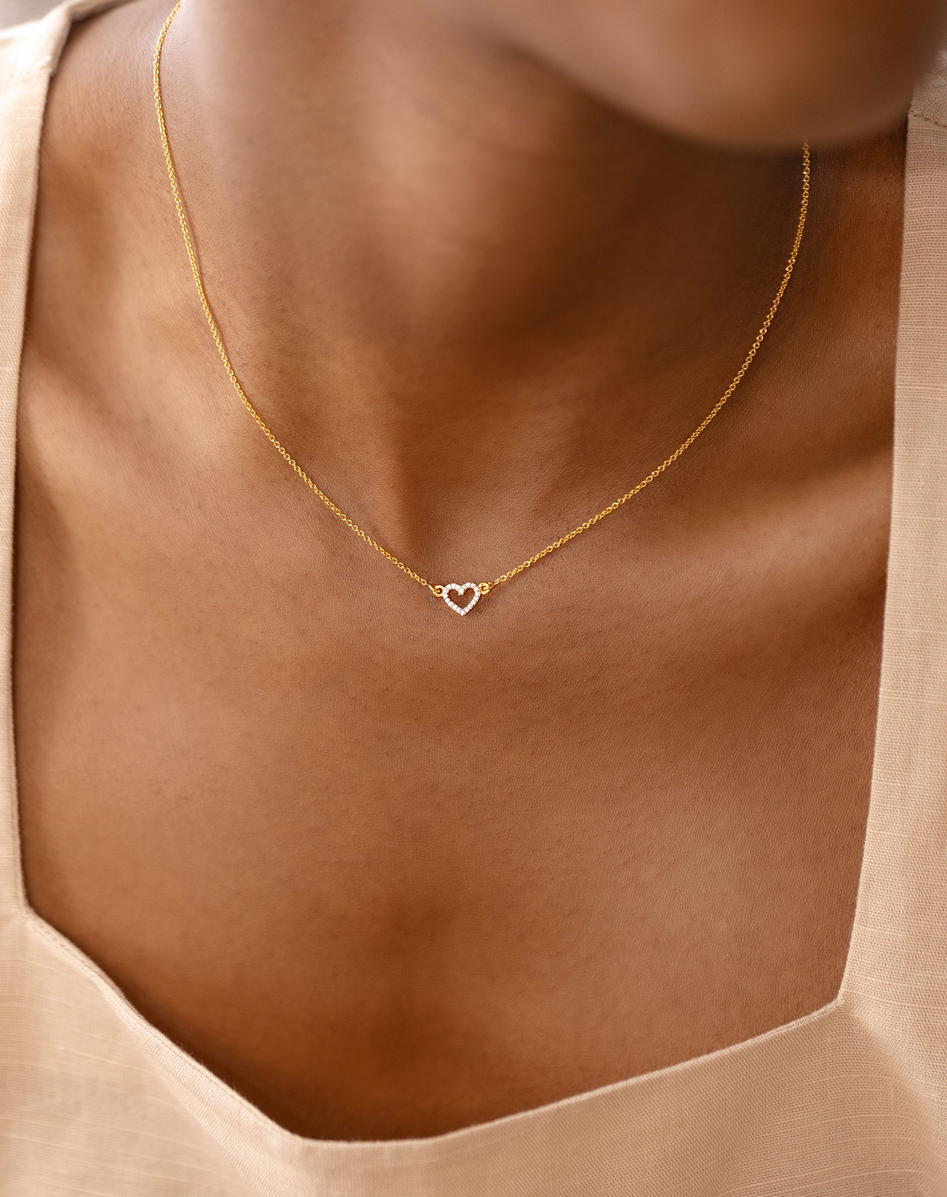 A close-up of a model wearing the gold Snap Heart Necklace, featuring a fine chain and a small, crystal-encrusted heart pendant.