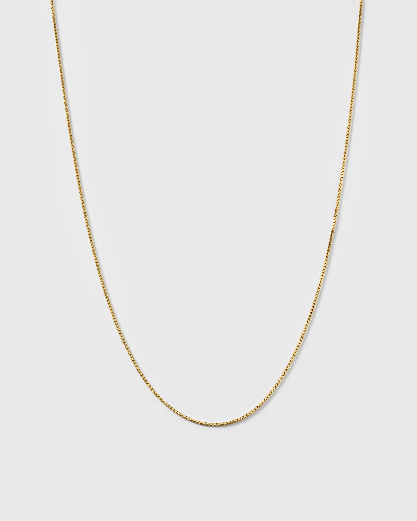 A product shot of the Beloved Long Box Chain in gold, hanging in a U-shape to display its fine box link design.