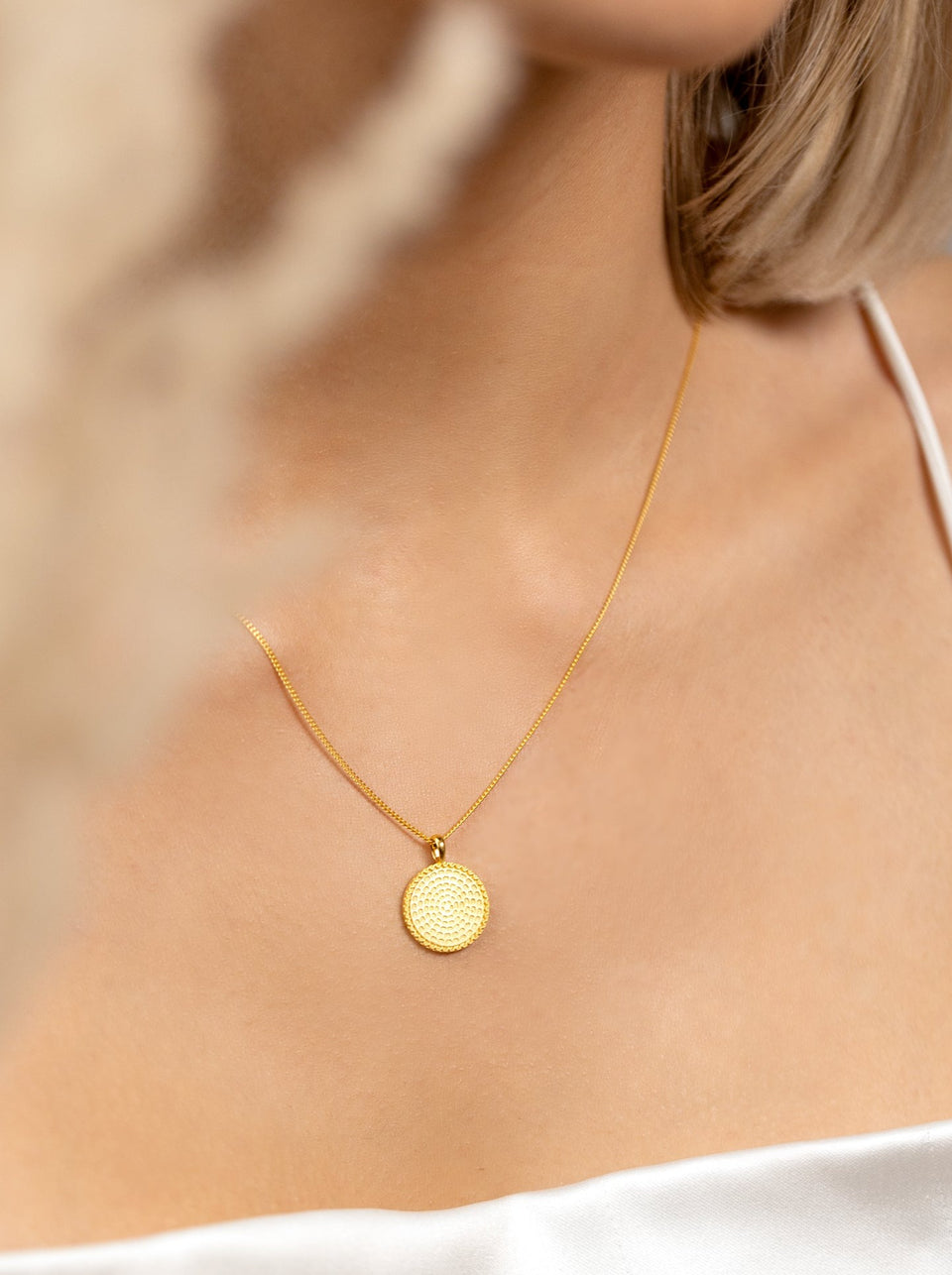 A close-up shot of a model wearing the Lucky Coin Heal Necklace in gold, featuring a delicate chain and a round pendant with a sun pattern.