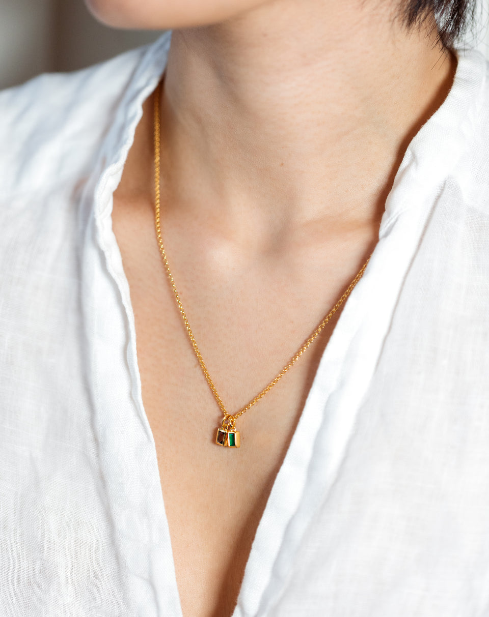 A close-up of a model wearing a Syster P gold necklace styled with two Beloved Squared Pendants, one with a green onyx and one with a smokey quartz stone.