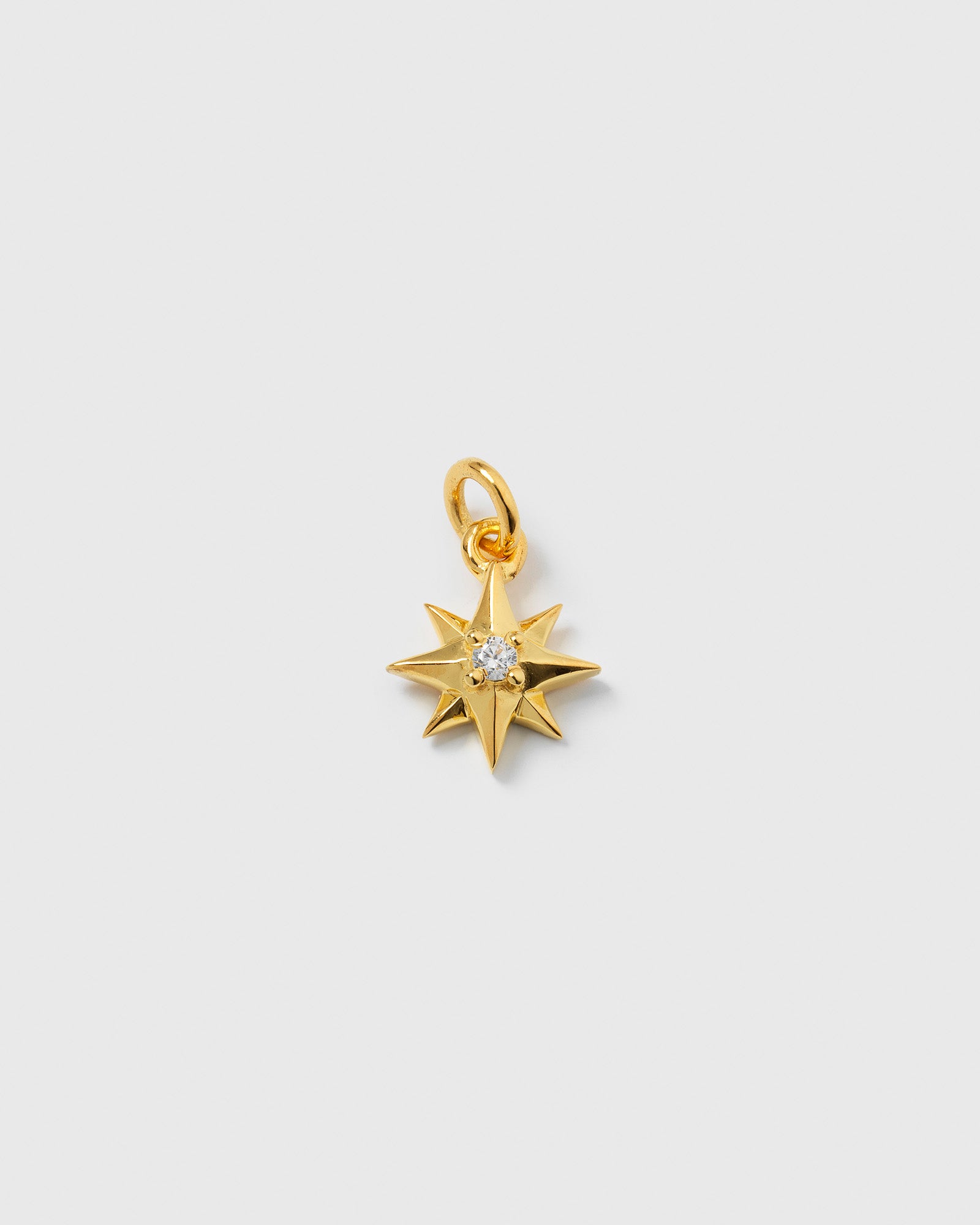 A product shot of the Beloved Compass Star Pendant in gold, featuring its compass star shape and a single cubic zirconia set in the center.