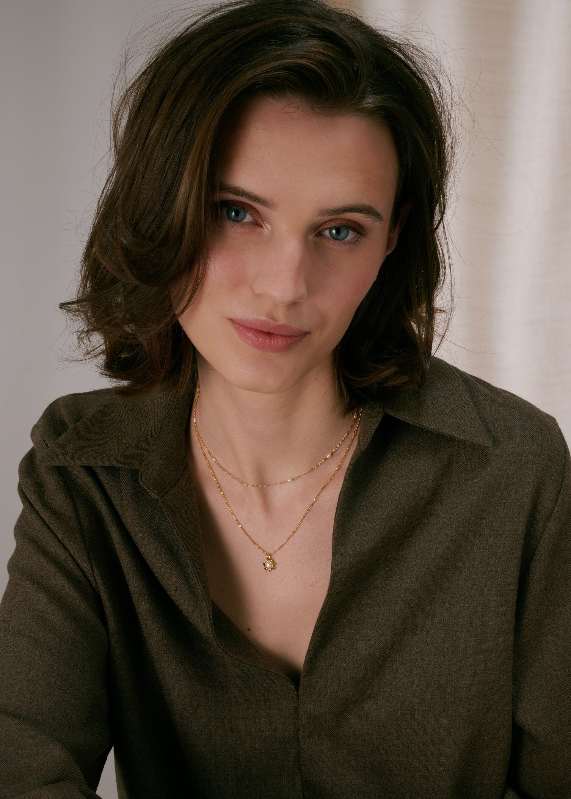 Two layered gold necklaces: a delicate chain with small spaced freshwater pearls, and a second chain with a sunburst pendant featuring a pearl in the center.