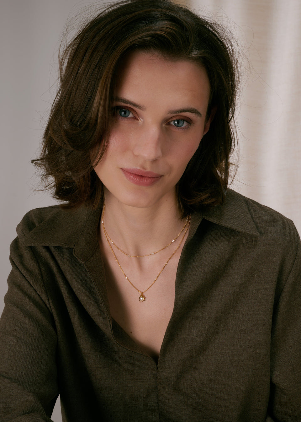 Two layered gold necklaces: a delicate chain with small spaced freshwater pearls, and a second chain with a sunburst pendant featuring a pearl in the center.