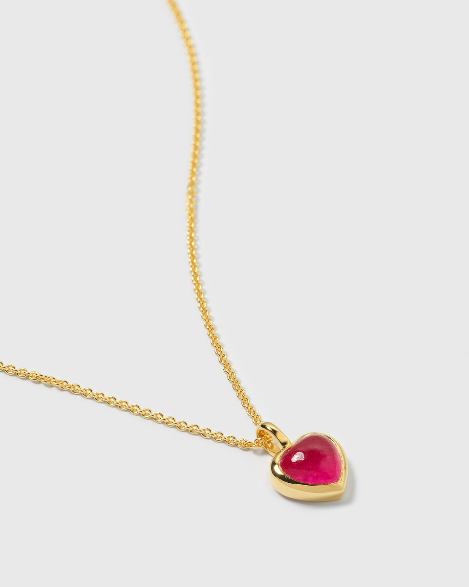 A close-up photo of the La La Love gold necklace, featuring a delicate chain and a heart-shaped pendant with a pink quartz stone.