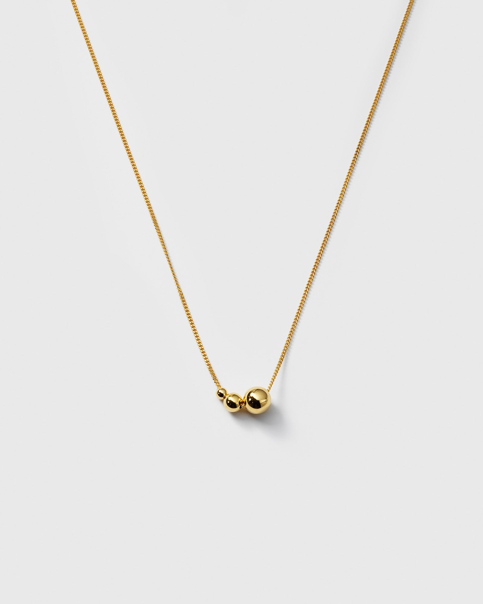 A product shot of the Universe Necklace in gold, featuring its fine chain adorned with three polished gold balls in varying sizes.