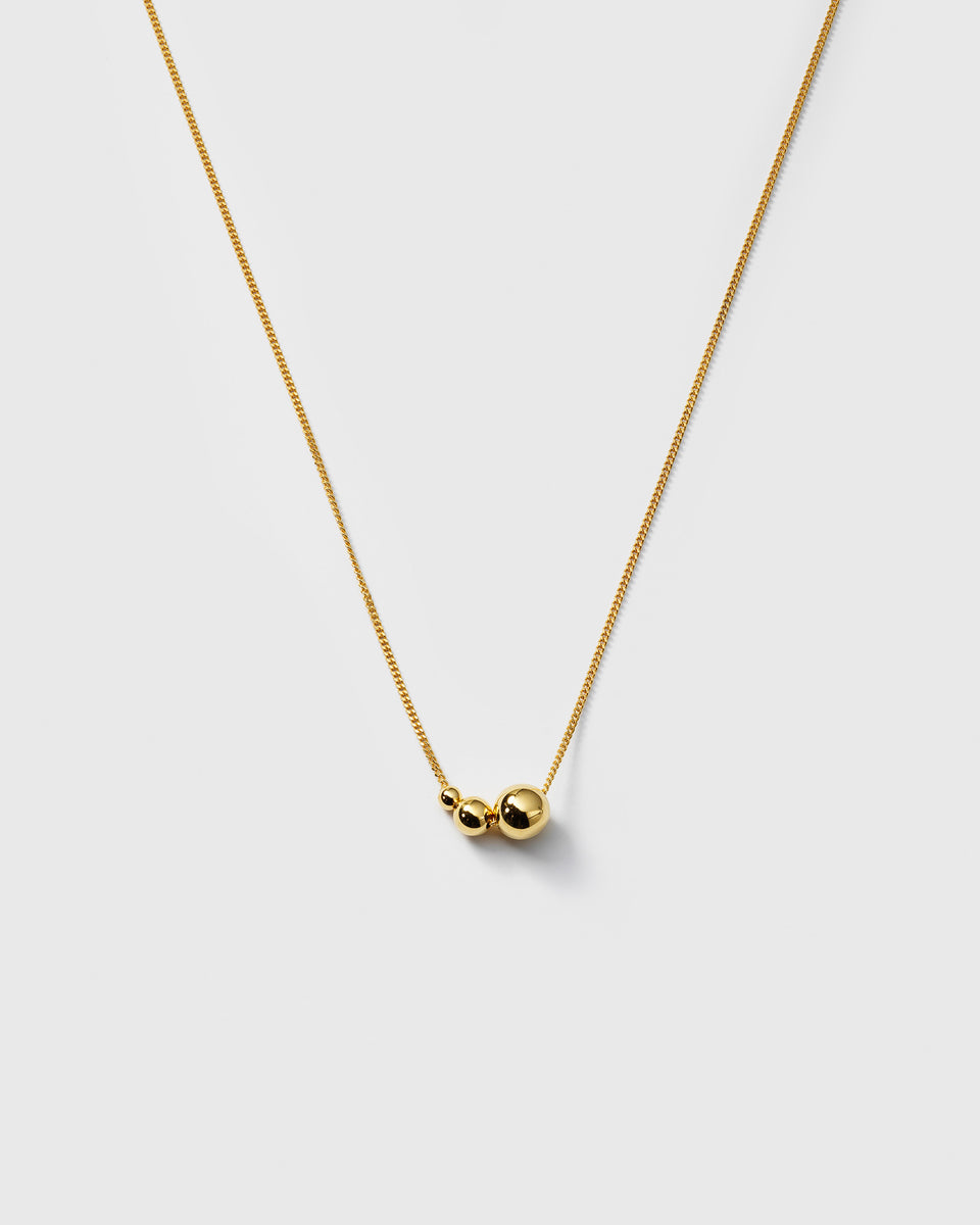 A product shot of the Universe Necklace in gold, featuring its fine chain adorned with three polished gold balls in varying sizes.