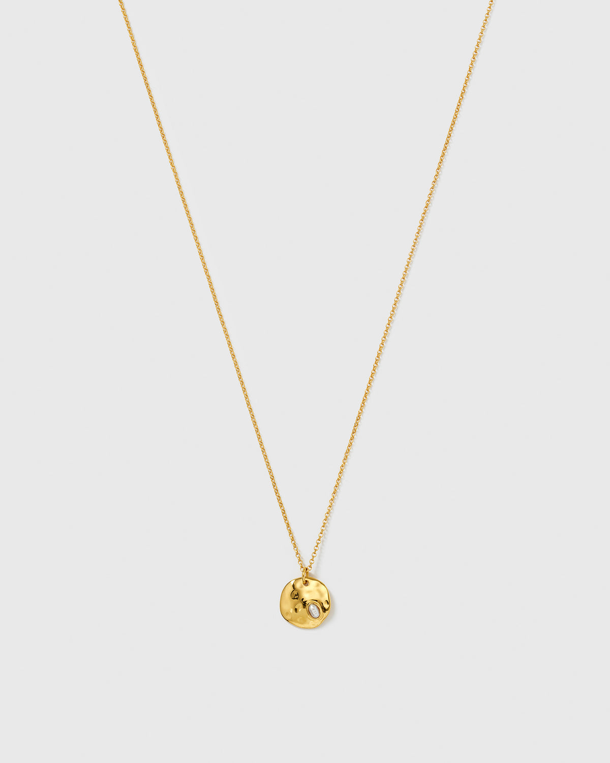 The Paxton Necklace Gold from Syster P, featuring a fine gold chain with a hammered, round pendant and an embedded baroque freshwater pearl.