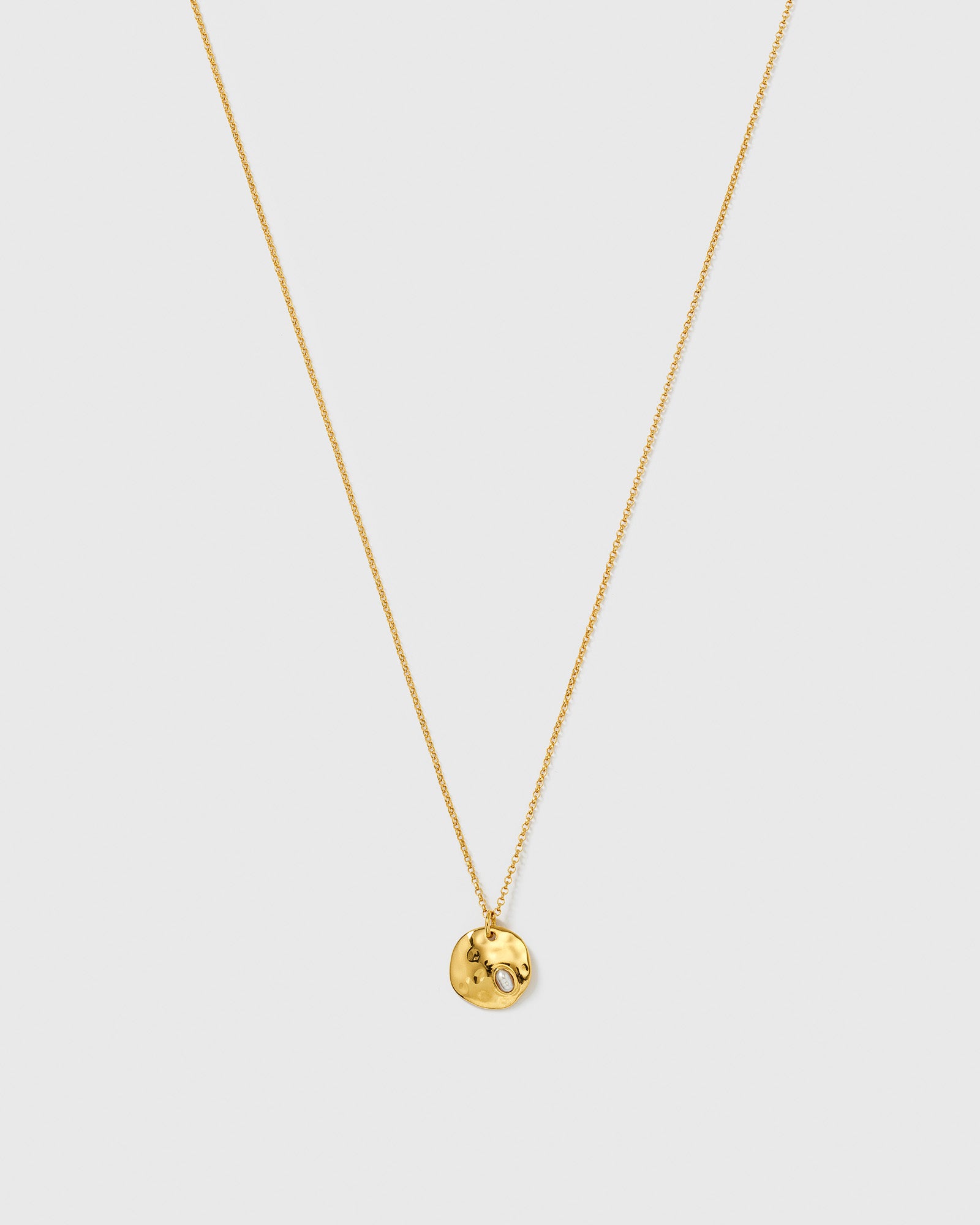 The Paxton Necklace Gold from Syster P, featuring a fine gold chain with a hammered, round pendant and an embedded baroque freshwater pearl.