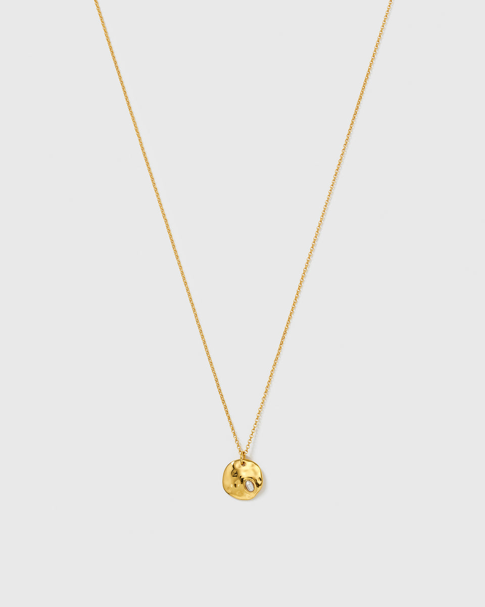 The Paxton Necklace Gold from Syster P, featuring a fine gold chain with a hammered, round pendant and an embedded baroque freshwater pearl.