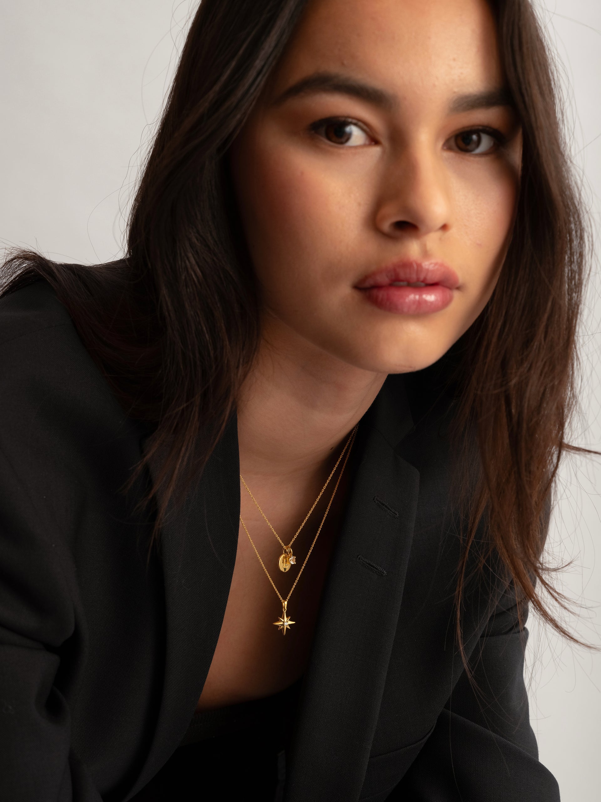 A gold necklace with a star-shaped pendant featuring a crystal, layered with a shorter gold chain.