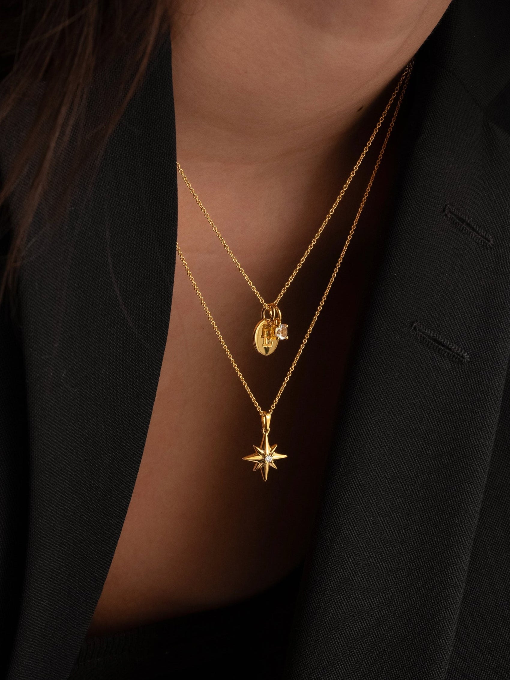 A model wears the gold Beloved Solo Nova Pendant, with its star-shaped charm, layered with another fine gold necklace featuring a round initial pendant and a white topaz charm.