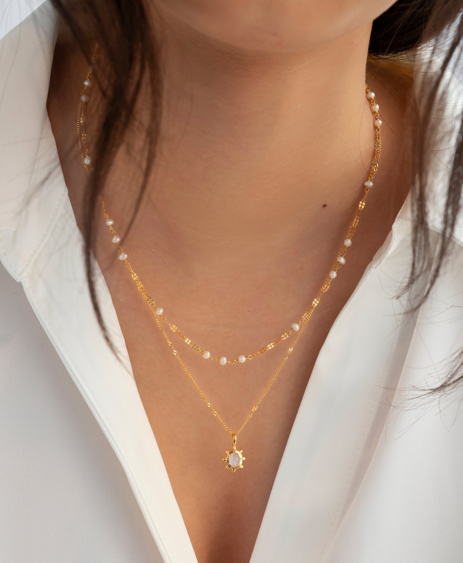 A close-up shot of a model wearing the Florentina Necklace in gold, featuring a flower-shaped moonstone pendant, layered with a second delicate gold necklace with small pearls.