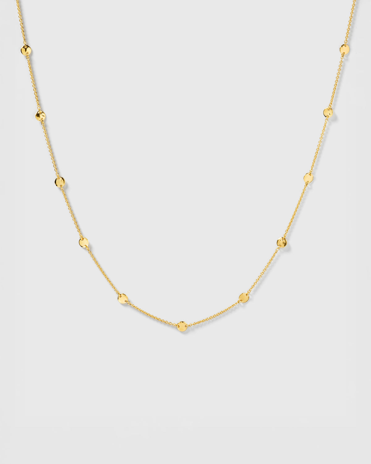 A product shot of the Solea Necklace in gold, laid out to showcase its design of a delicate chain adorned with small, round, hammered circles.