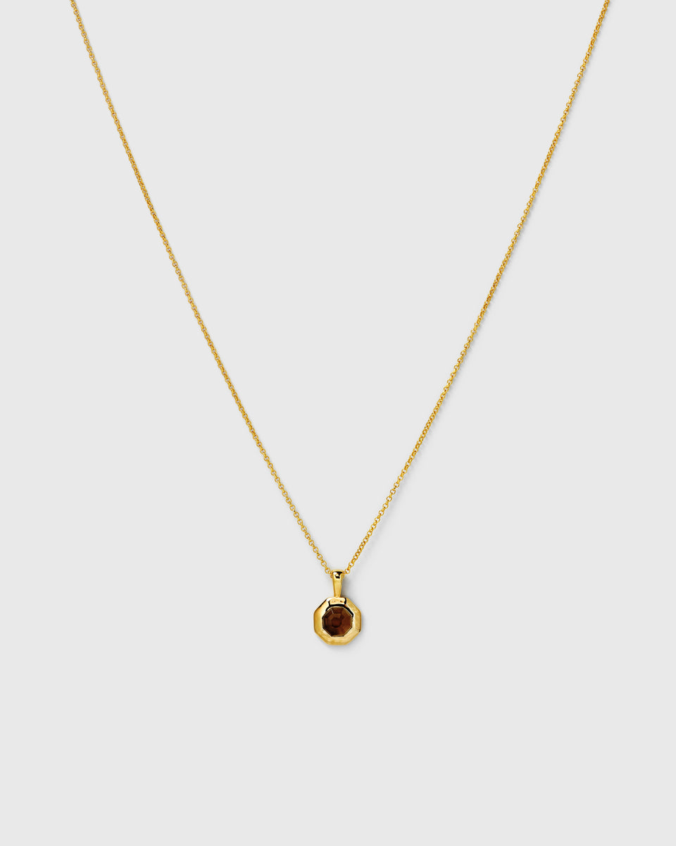 A necklace in gold, featuring a fine chain and an octagonal pendant set with a faceted smokey quartz stone.