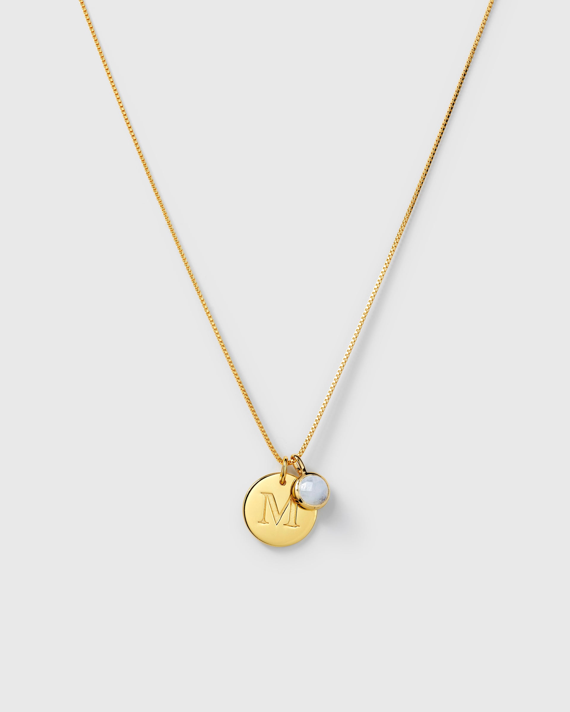 Gold necklace with two pendants: a round aquamarine March birthstone and a round letter charm.