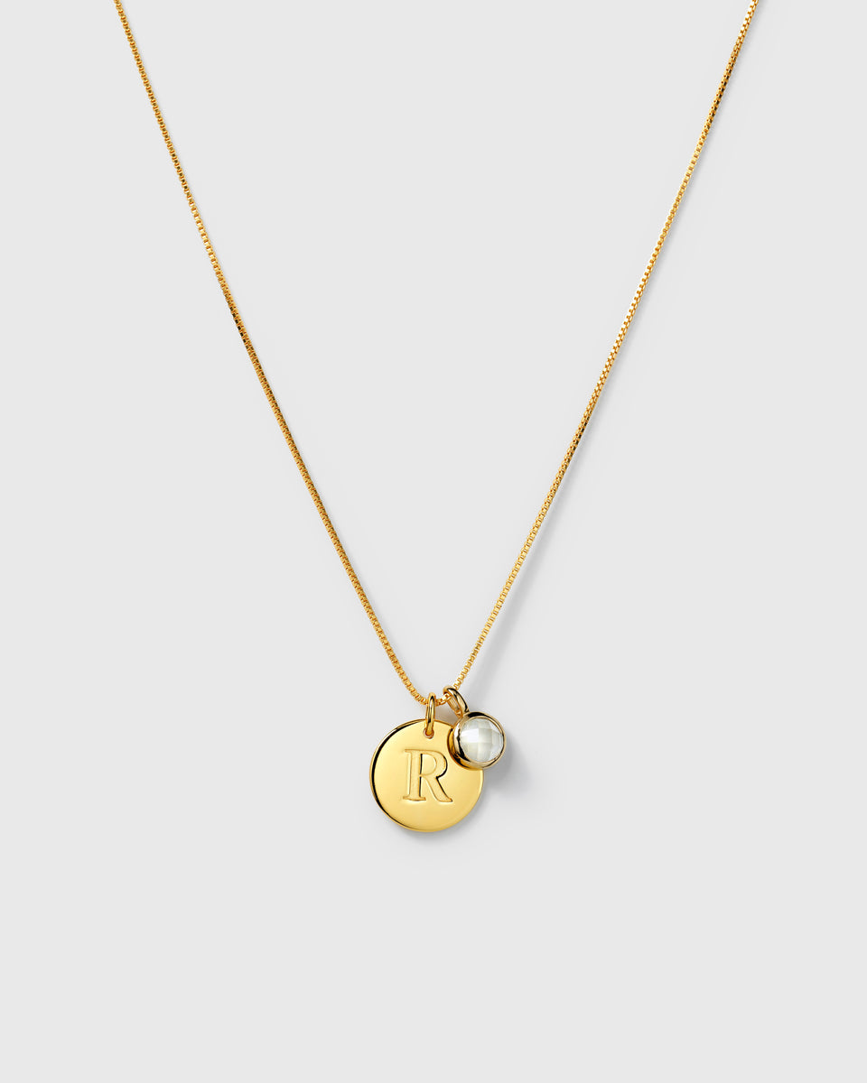 Gold box chain necklace with two pendants: a round letter charm and a round faceted moonstone. 