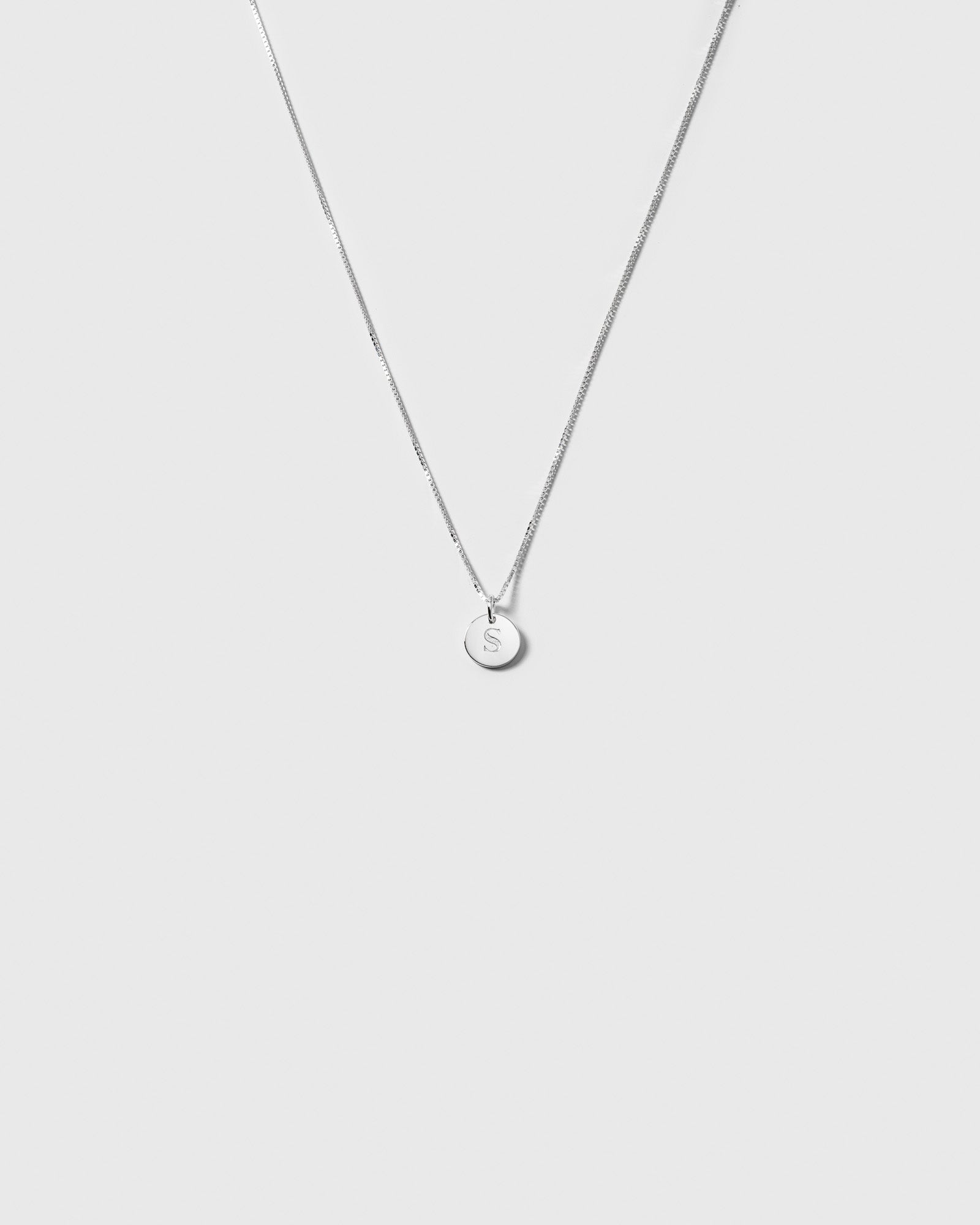A product shot of the Beloved Short Box Chain in silver, paired with a small, round pendant engraved with the letter 'S'.