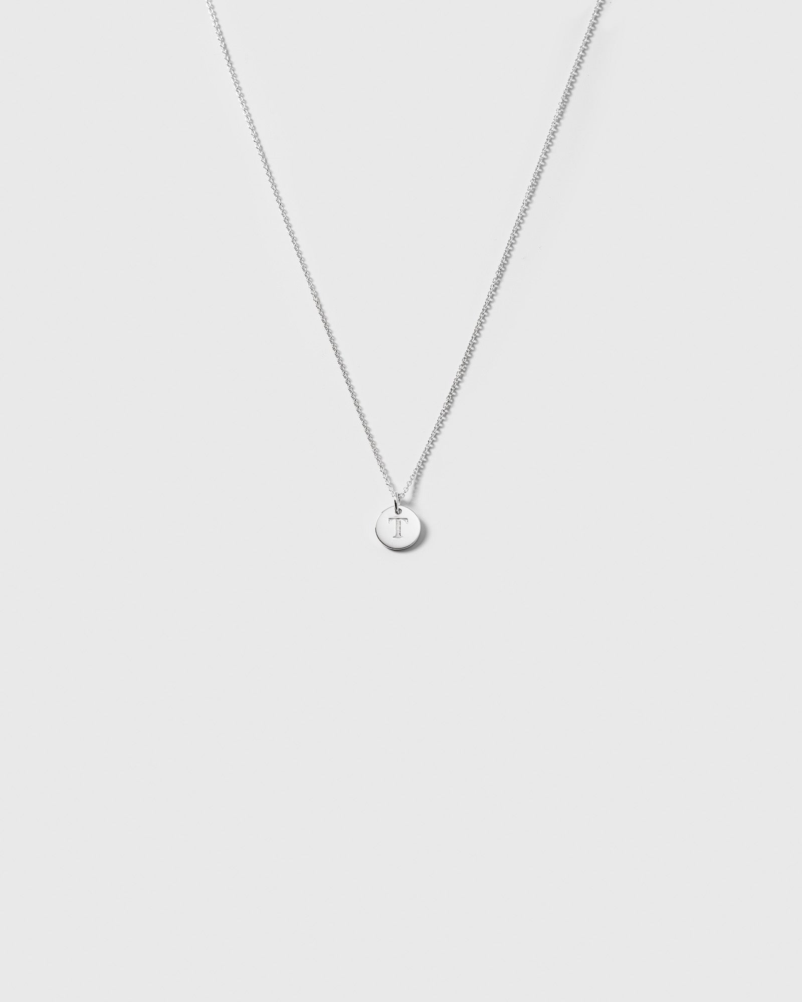 A product shot of the Beloved Short Oval Chain in silver, styled with a small, round pendant engraved with the letter 'T'.