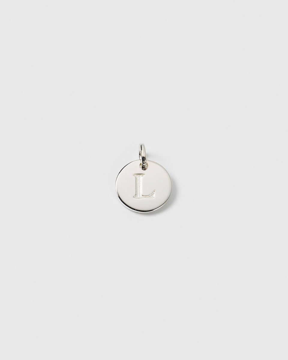 A product shot of the Syster P Beloved Mini Letter charm in silver, a round pendant with the initial 'L' engraved on its polished surface.