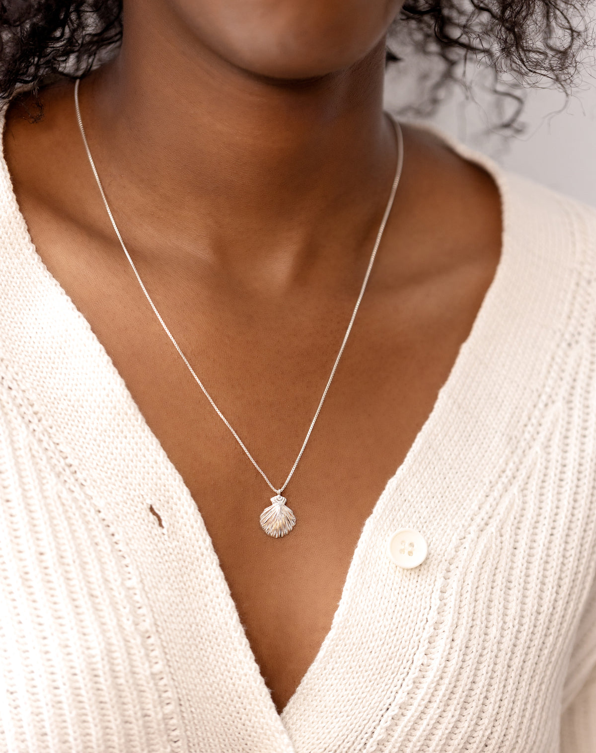 A close-up shot of a model wearing the Beaches Shell Necklace in silver, featuring its fine chain and detailed, shell-shaped pendant.
