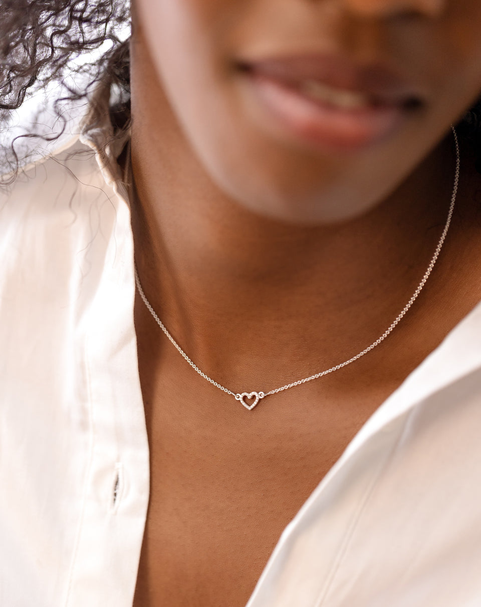 A close-up shot of a model wearing the Snap Heart Necklace Silver Crystal, featuring a fine silver chain and a delicate heart-shaped pendant covered in sparkling crystals.