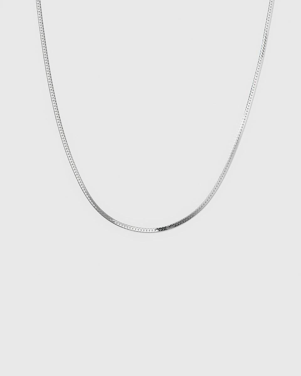 A product shot of the Herringbone Necklace in silver, highlighting its smooth and flat chain design.