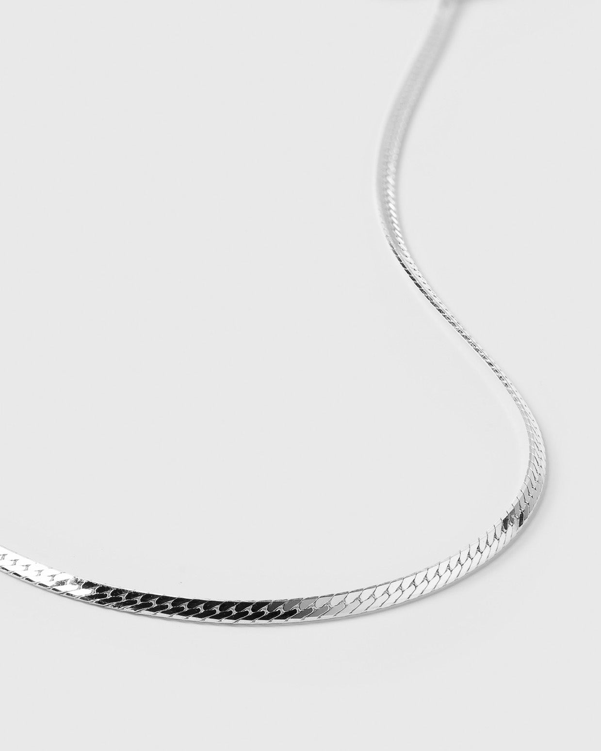A close-up shot of the Herringbone Necklace in silver, highlighting its smooth, flat chain and intricate herringbone pattern.