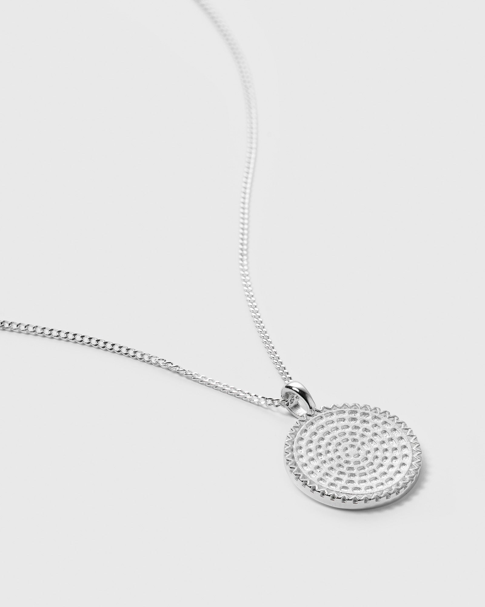 A close-up product shot of the Lucky Coin Heal Necklace in silver, showing the back of the textured, round pendant with the word "heal" engraved on it.