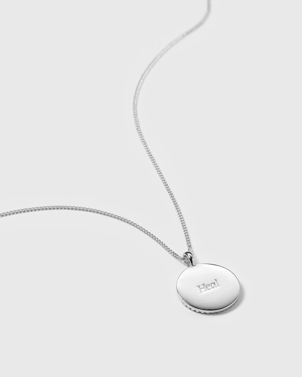 A product shot of the Lucky Coin Heal Necklace in silver, featuring its fine chain and the back of the coin pendant engraved with the word "Heal".