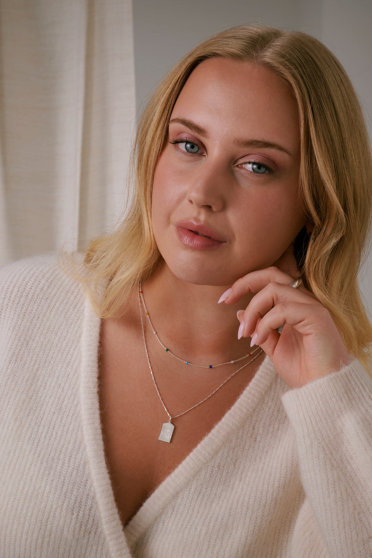 Santa Monica Necklace in silver, showcasing its delicate chain adorned with small, colorful gemstones. Layered with a longer silver necklace showcasing its fine chain and rectangular pendant engraved with a sun and waves design.