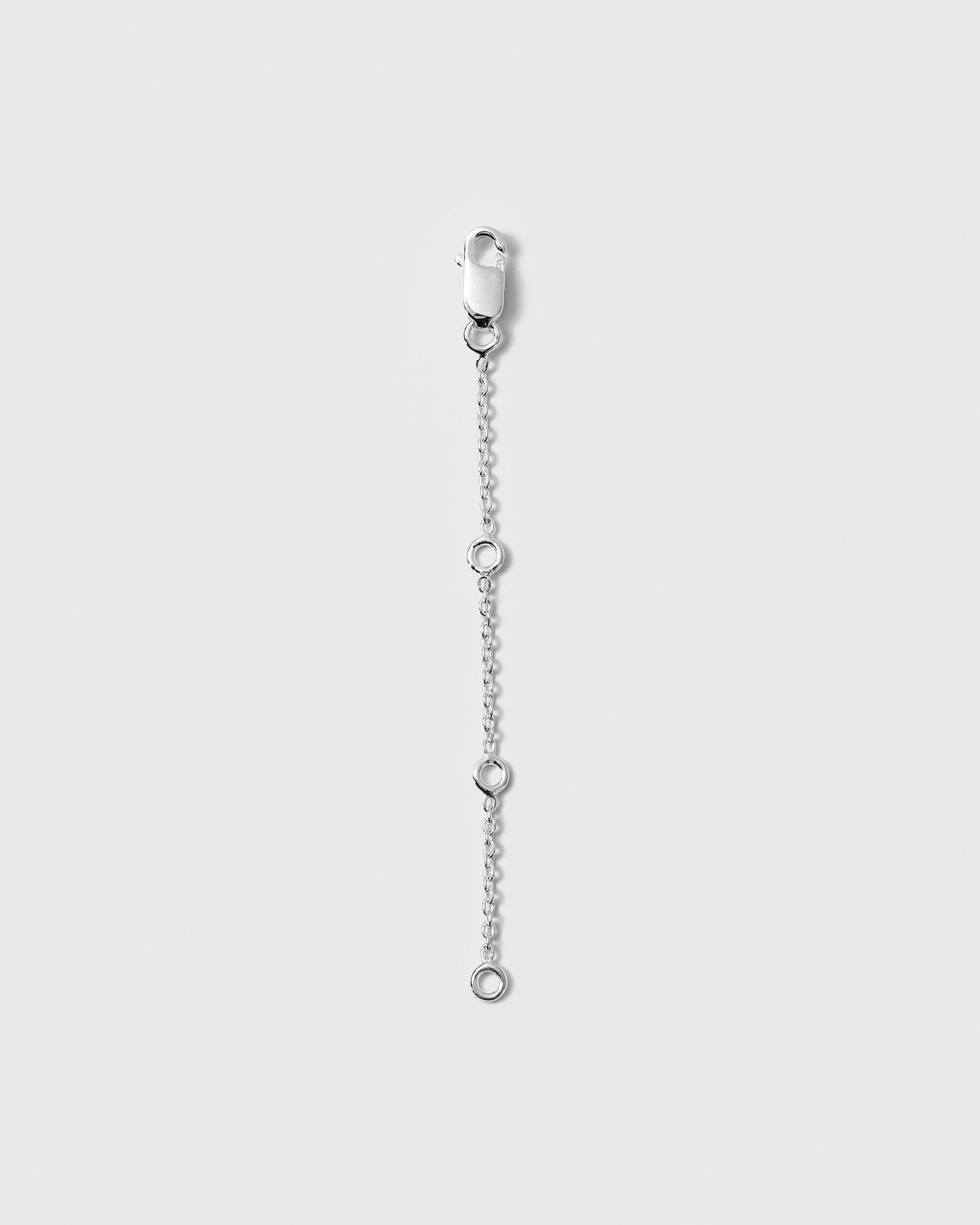 A product shot of the Extension Chain in silver, showing its fine chain with three adjustable closing rings and a lobster clasp.