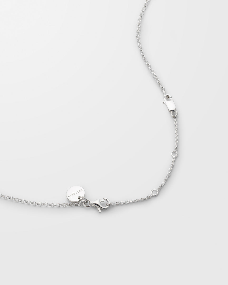 A detailed product shot of the Syster P Extension Chain in silver, showing how it attaches to a necklace to provide adjustable length with its multiple loops.