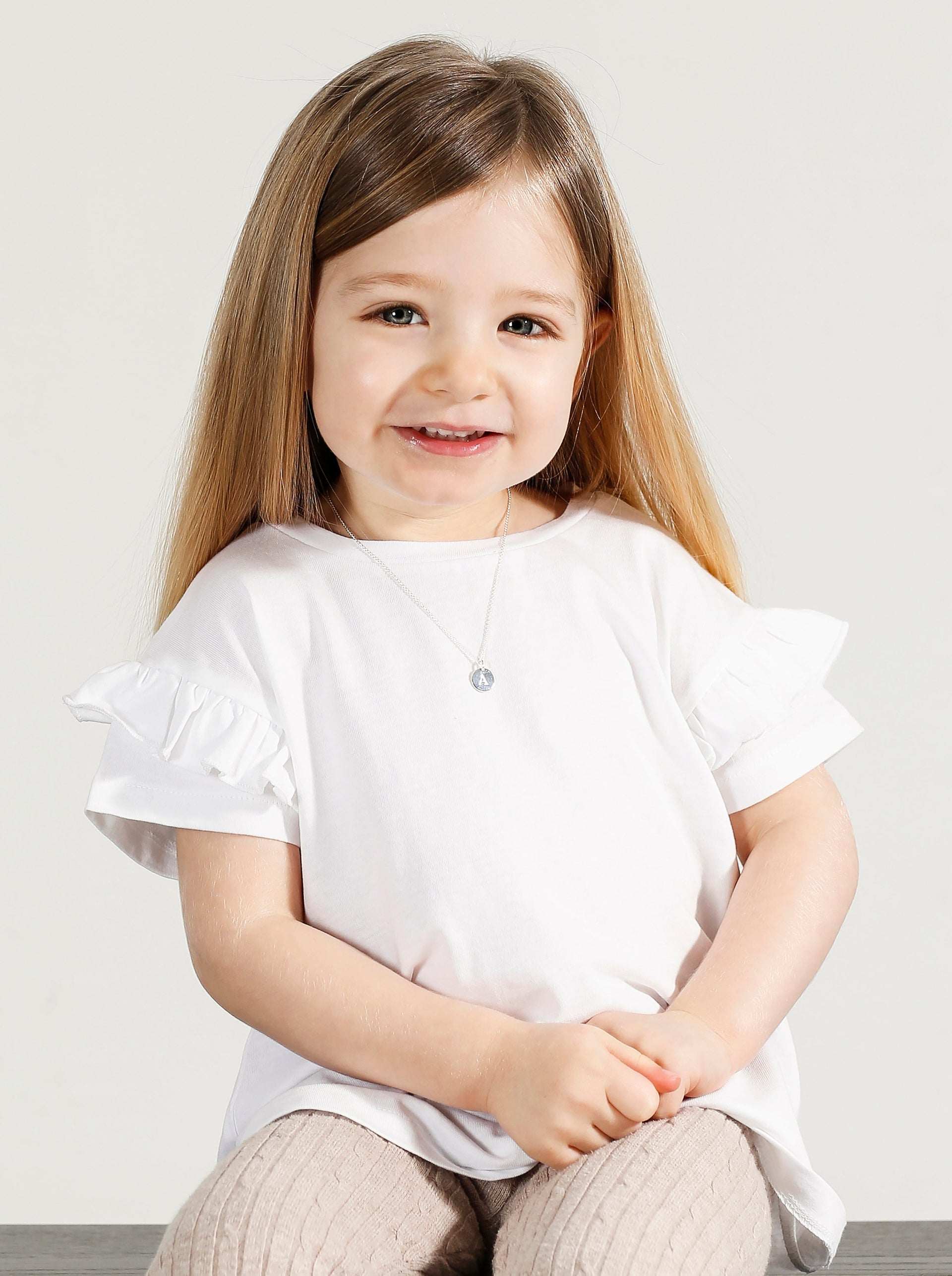 A model shot of a young girl wearing the Beloved Baby Chain Silver, styled with a small, round letter 'A' pendant.