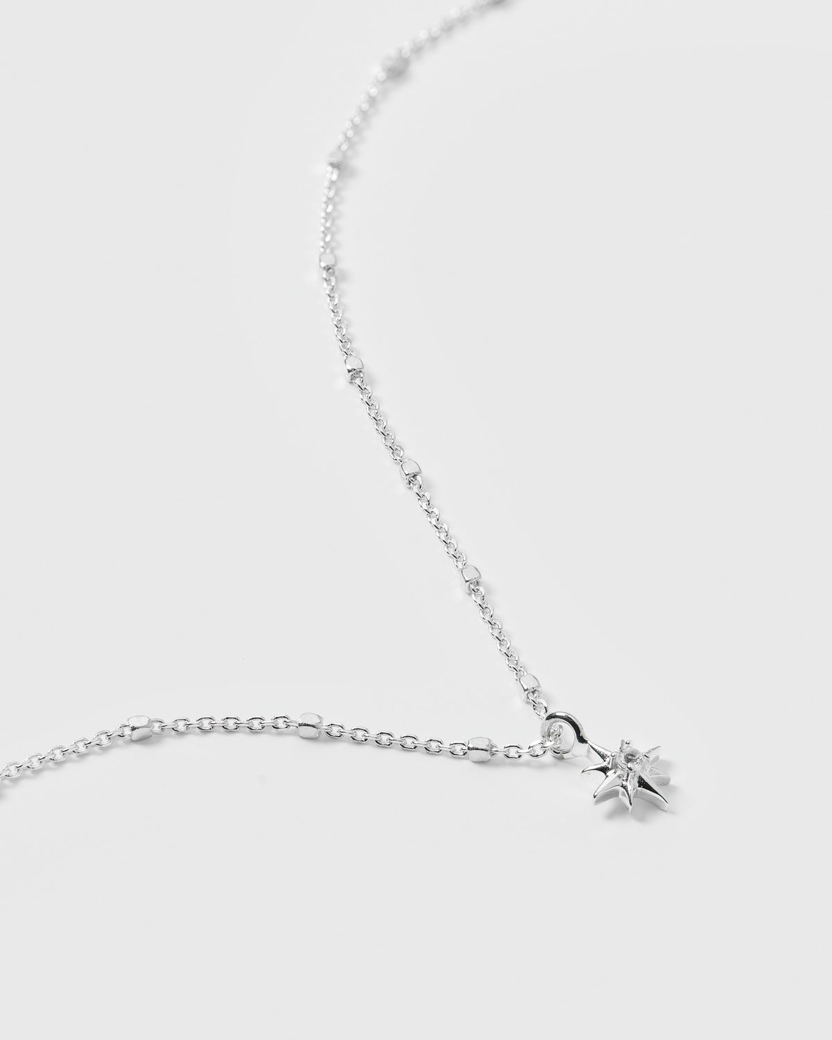 A close-up product shot of the North Star Necklace in silver, showcasing the intricate detail of its unique chain and the star pendant with a central crystal.