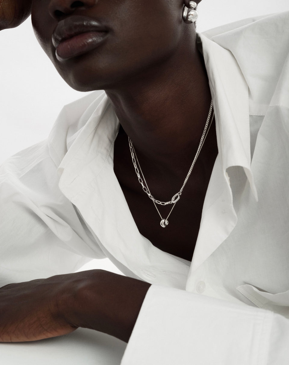 A close-up shot of a model wearing the Harvey Heavy Necklace in silver, which features a unique design combining two different types of chains. She is also wearing a chunky silver earring.