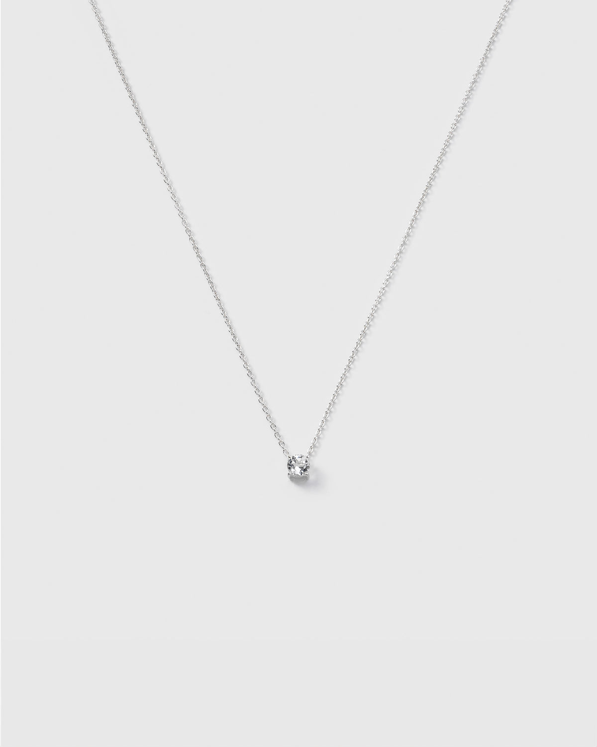 A product shot of the Minimalistica Solo Nova Necklace in silver, featuring its thin, delicate chain and a small, round white topaz stone in a simple setting.